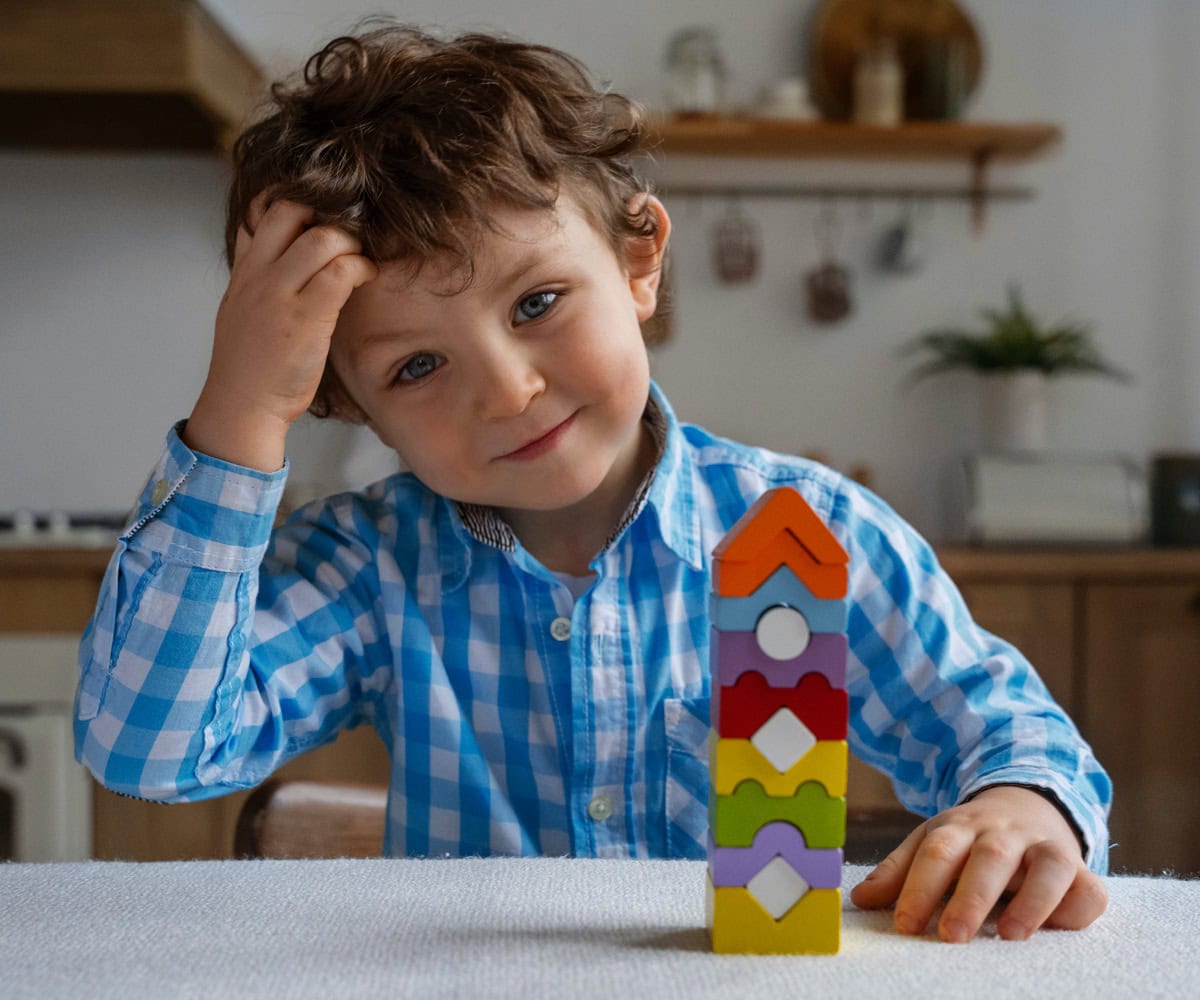 Giovane bambino che gioca con torri di blocchi colorati in cucina, immagini di gioco e creatività infantile, ambiente domestico accogliente e sicuro, stimolazione mentale e sviluppo delle capacità motorie.